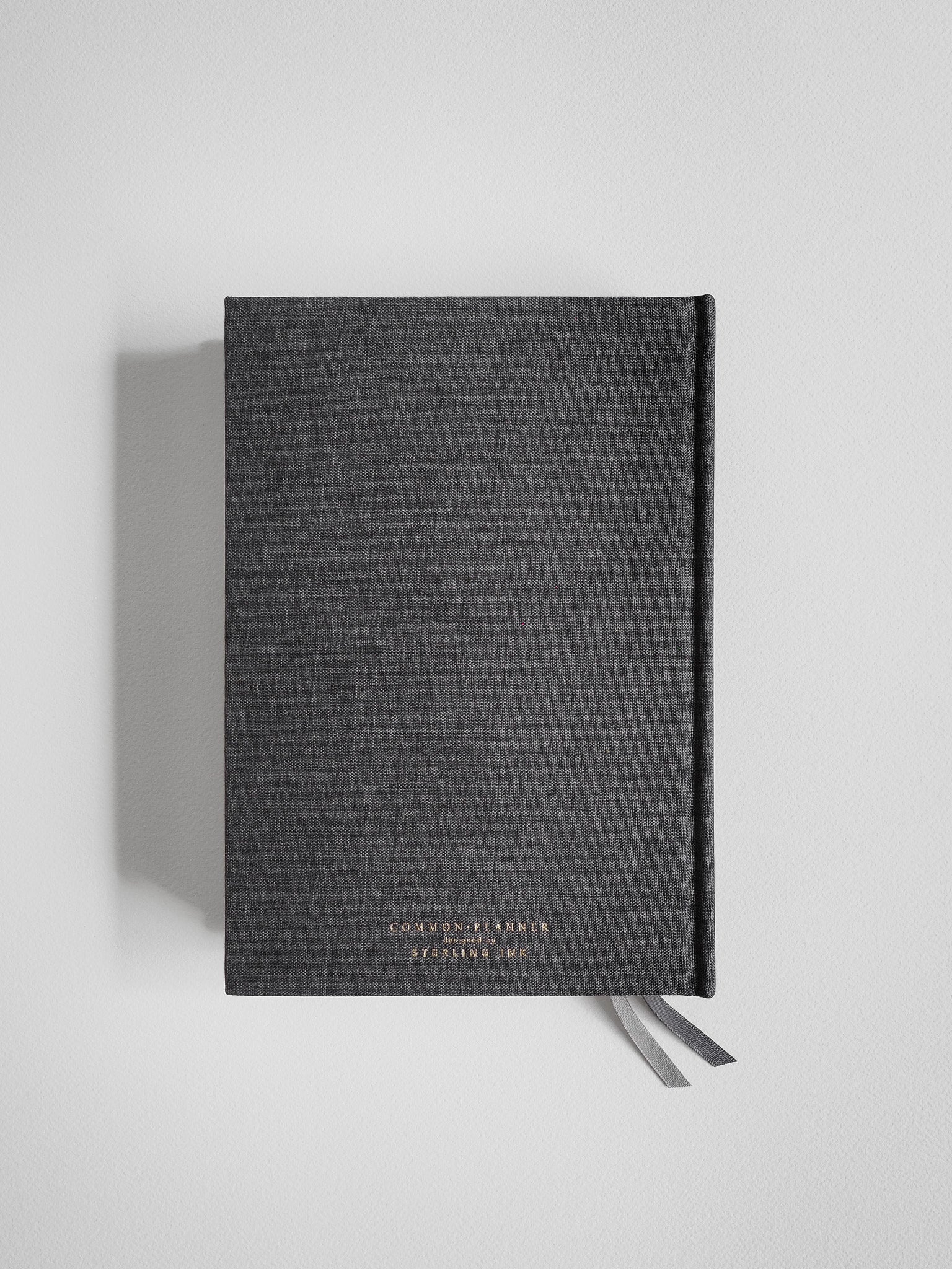 Dark charcoal A5 academic planner with a fabric cover, branded with "Common Planner," and featuring a decorative ribbon closure for organization.