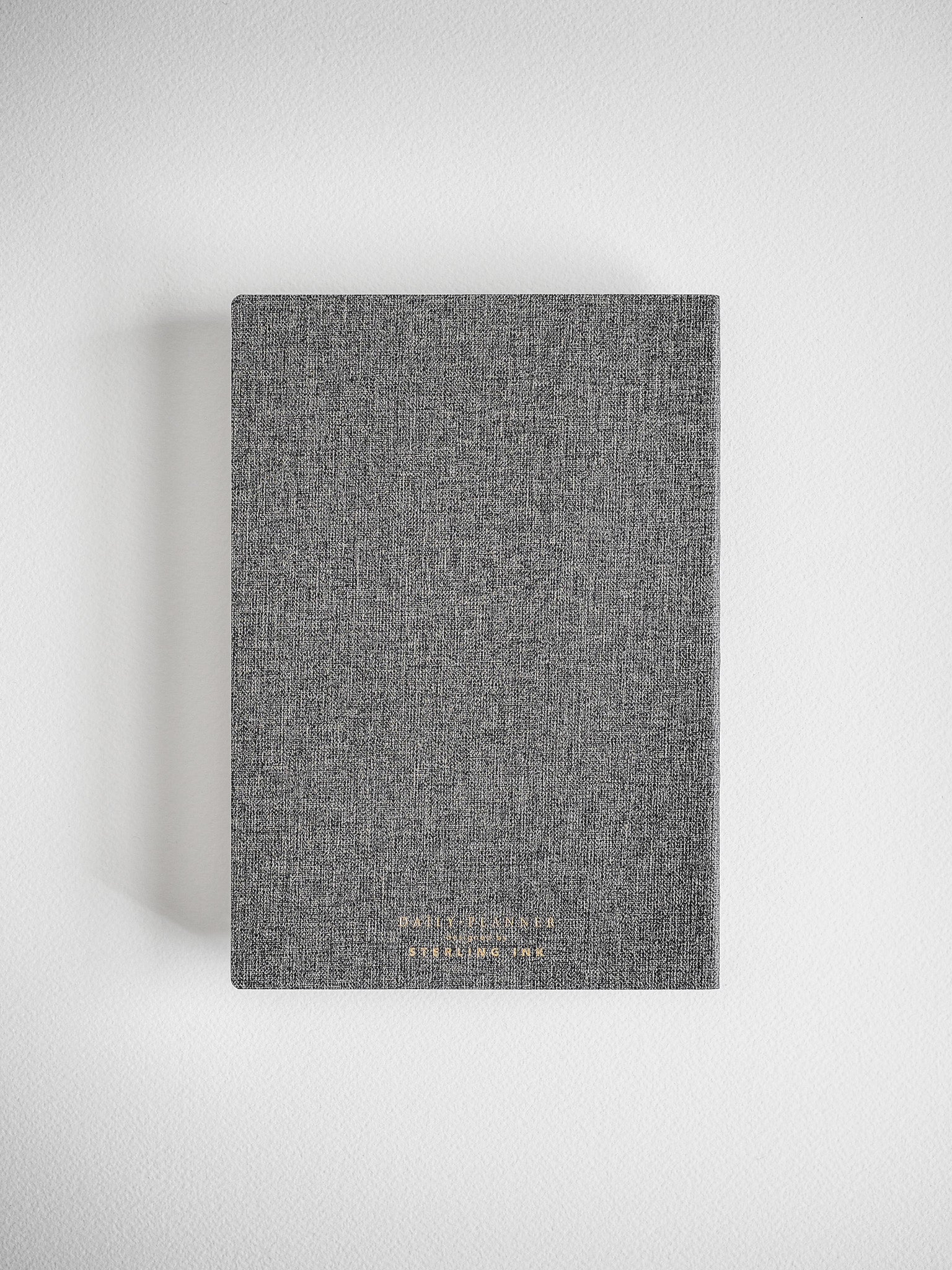 Dark charcoal gray daily planner with a subtle textured finish and elegant gold foil lettering displaying the year and 'Daily Planner' title.