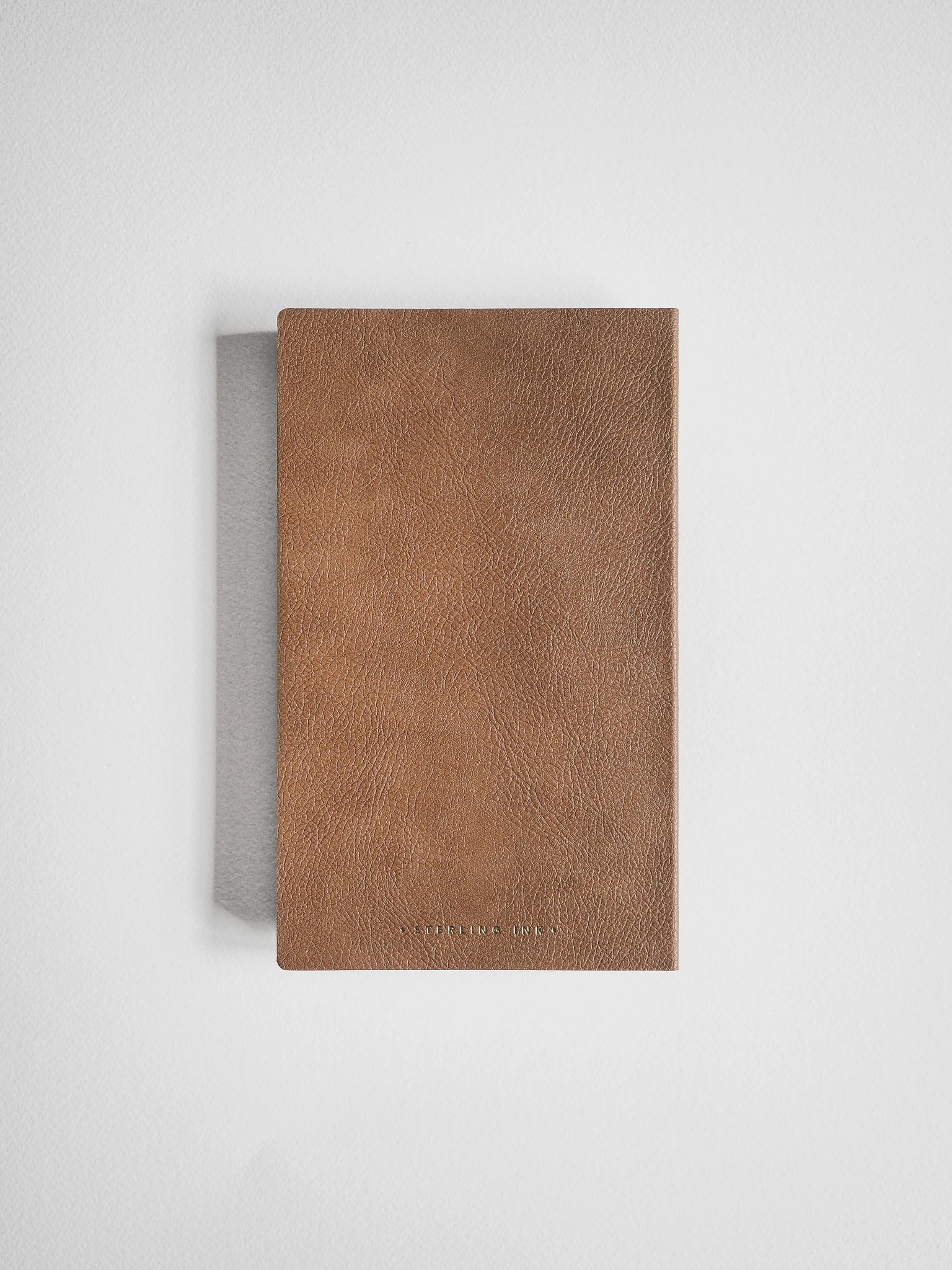 A brown textured leather notebook or journal with a thin gray fabric spine, shown from a top-down view on a light gray background.
#Color_Caramel