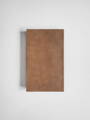 A brown textured leather notebook or journal with a thin gray fabric spine, shown from a top-down view on a light gray background.
#Color_Caramel