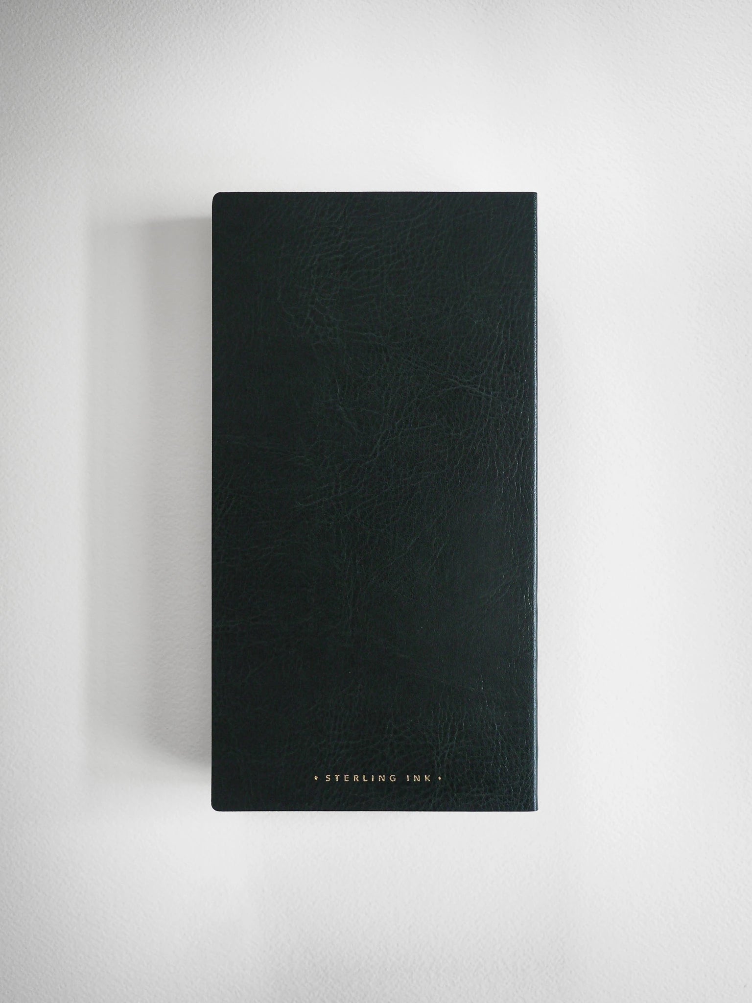 A tall, dark green textured leather journal or notebook with gold foil text reading 'STERLING INK.' at the bottom, displayed against a neutral light gray background.
#Color_Forest