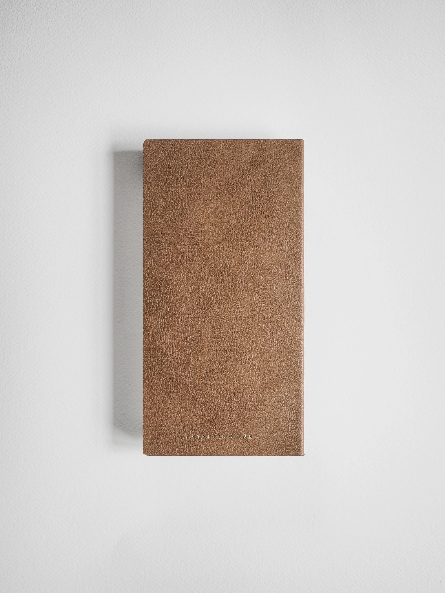 A brown textured leather notebook or journal with a clean, minimalist cover, shown vertically against a light gray background.
#Color_Caramel