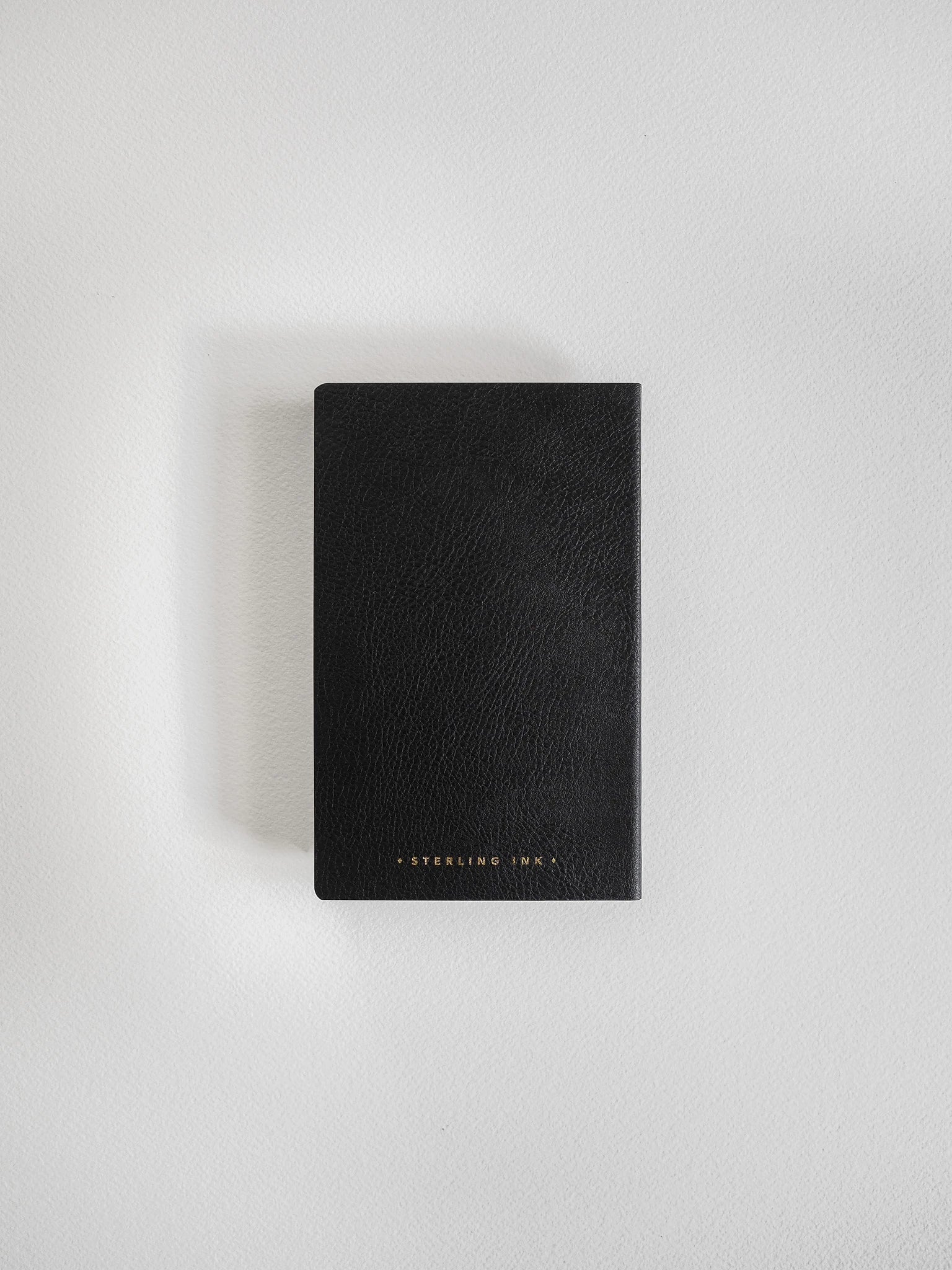 A black textured leather notebook or journal with gold foil 'STERLING INK.' branding at the bottom, shown flat on a light gray background.
#Color_Onyx
