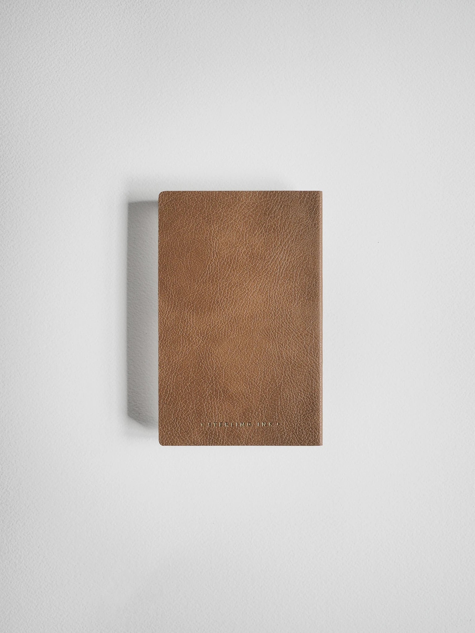 A slim, rectangular brown leather notebook or journal with a textured leather cover, shown against a plain light gray background.
#Color_Caramel