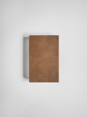 A slim, rectangular brown leather notebook or journal with a textured leather cover, shown against a plain light gray background.
#Color_Caramel
