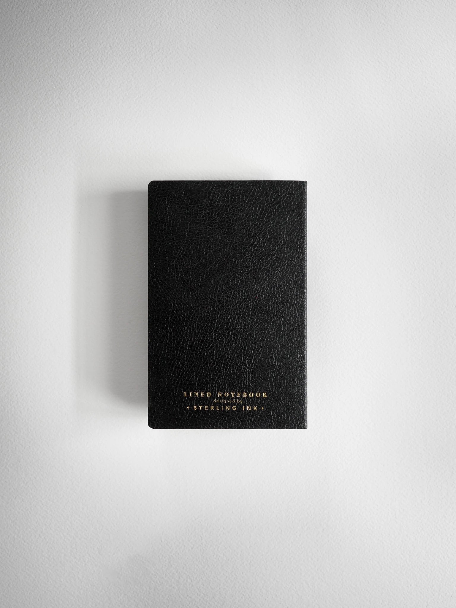 A black textured leather-bound notebook with gold foil lettering on the bottom, centered against a light gray background.
#Color_Onyx