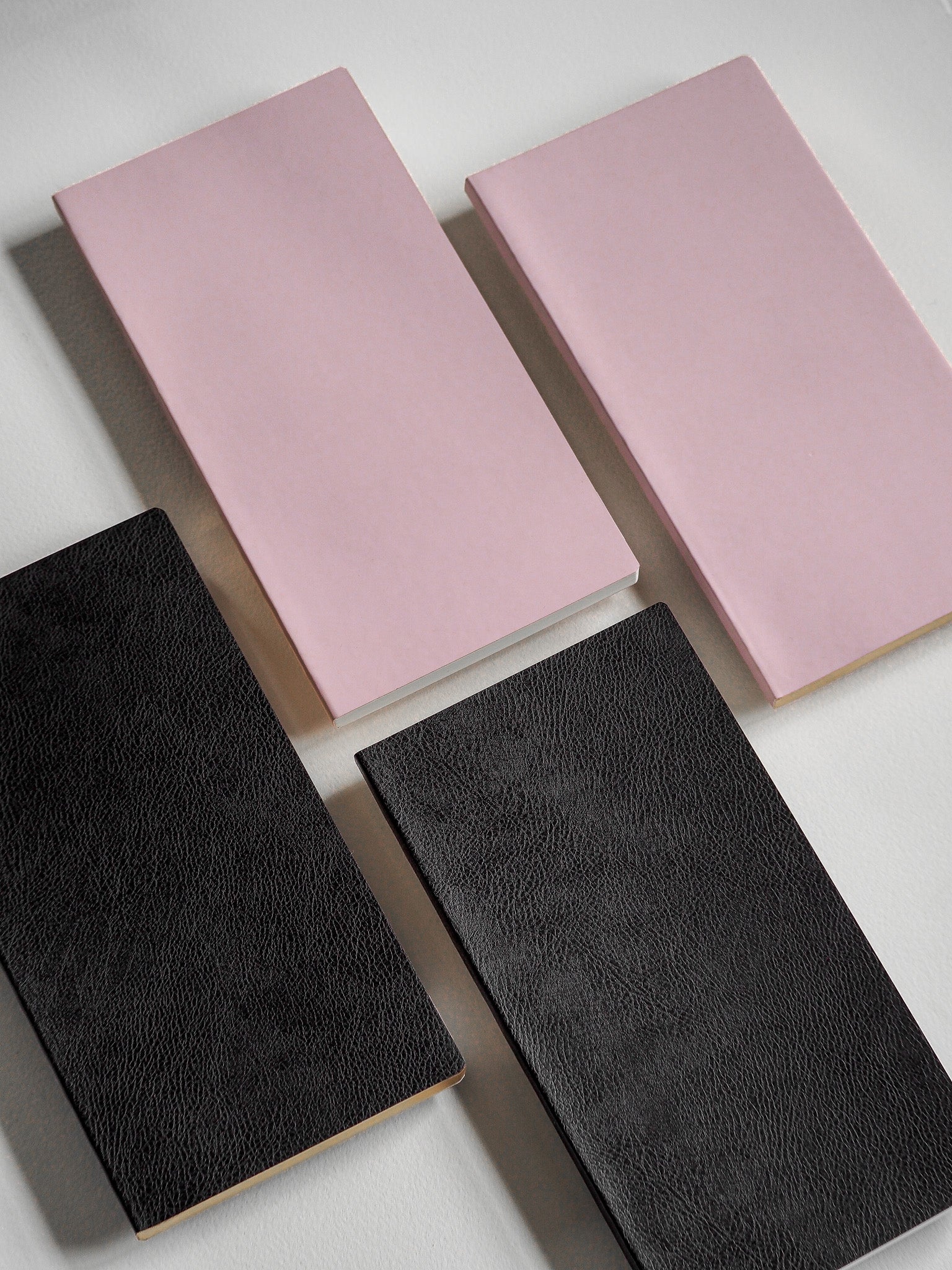 Solid color notebooks displayed in soft blush pink and deep charcoal gray covers, ideal for grid journaling and planning.