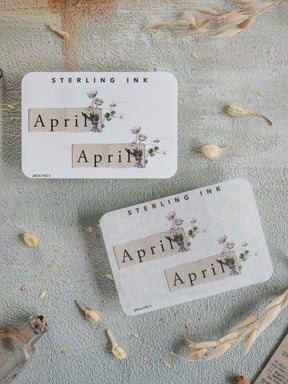 Botanical April month planner stickers featuring the text "April" and "Sterling Ink," adorned with delicate watercolor greenery and spring florals.