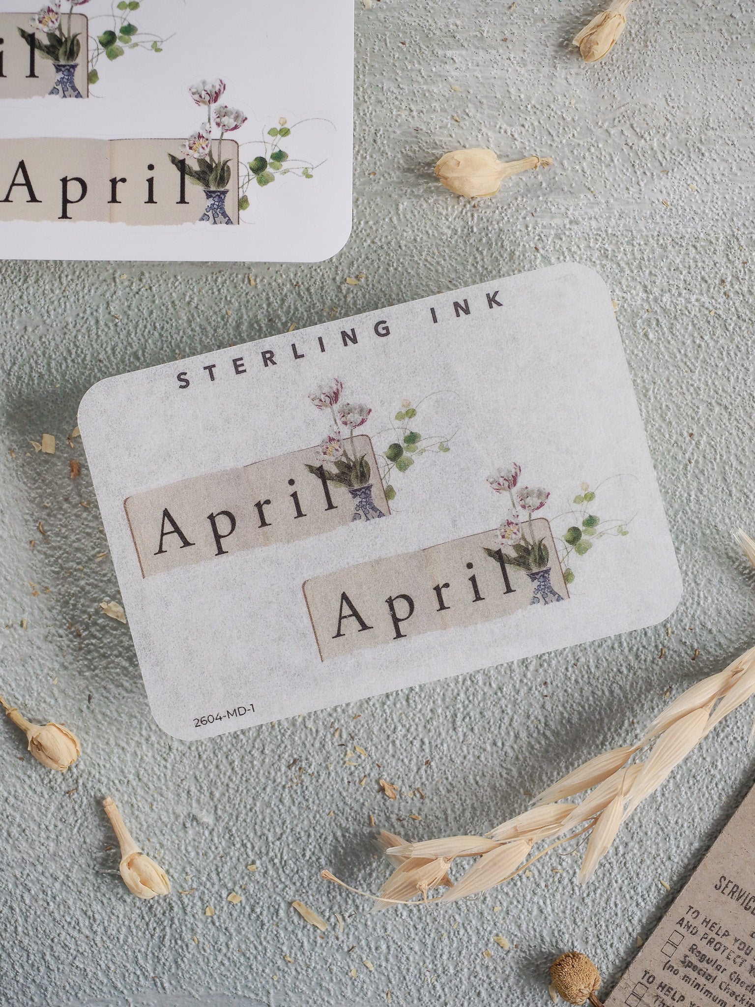 Pastel spring floral stickers featuring the word "April" framed by delicate watercolor illustrations of greenery and soft pink and purple blooms.