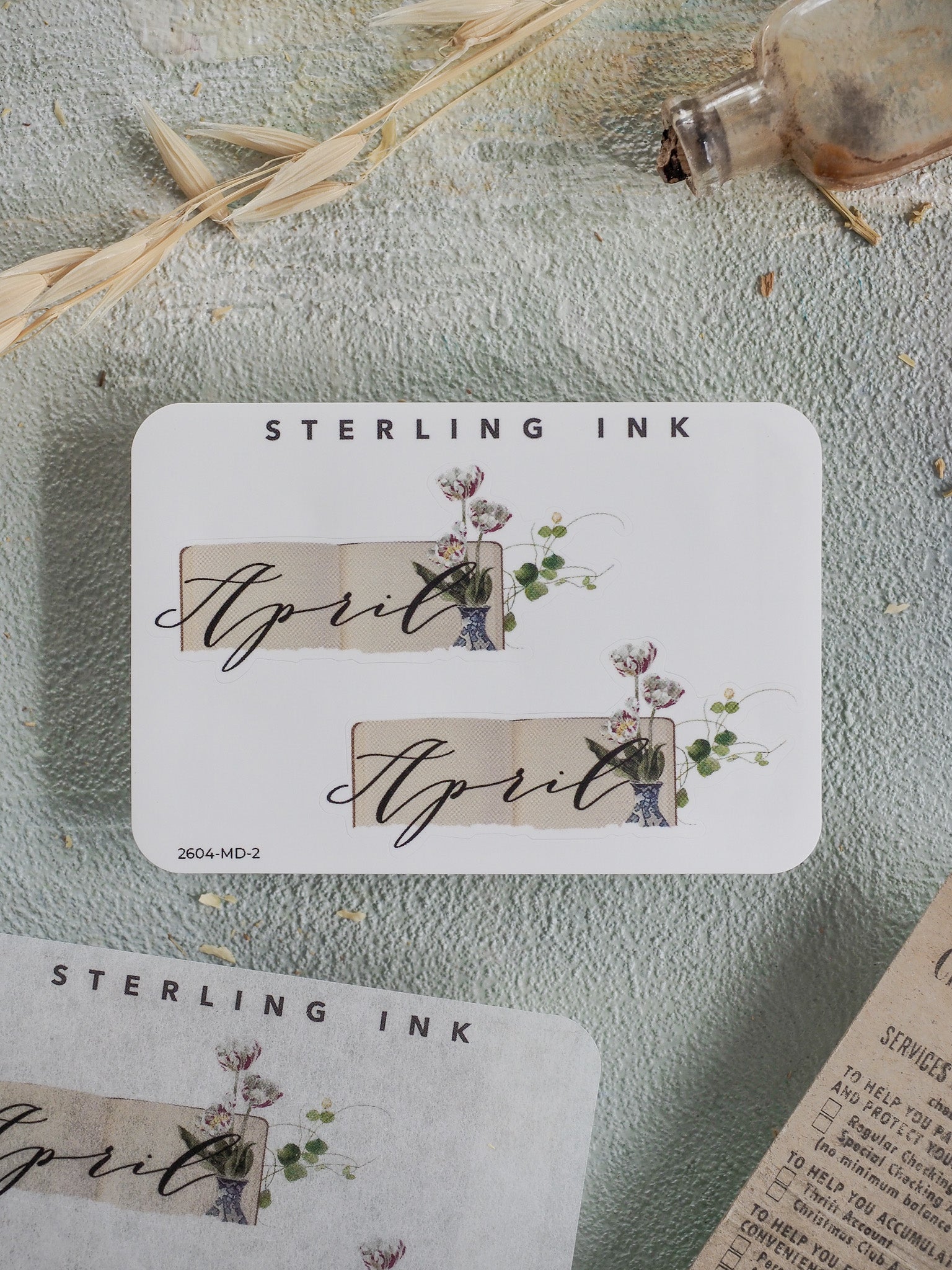 Elegant April month sticker featuring a soft cream background, script "April" text, and delicate watercolor illustrations of natural blooms and greenery.