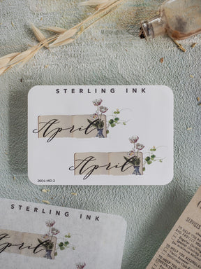 Elegant April month sticker featuring a soft cream background, script "April" text, and delicate watercolor illustrations of natural blooms and greenery.