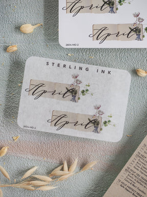 Elegant April month sticker set featuring the name in gold script, set against a cream background with delicate botanical illustrations of blush pink flowers and soft greenery.