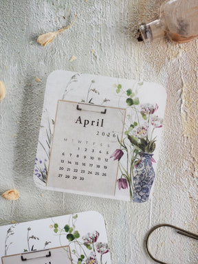 Detailed monthly calendar for April 2026 featuring a delicate watercolor design of spring flowers and a charming blue vase illustration.