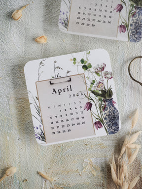 Elegant April 2026 calendar card featuring soft watercolor illustrations of purple and green botanical flowers and natural foliage.