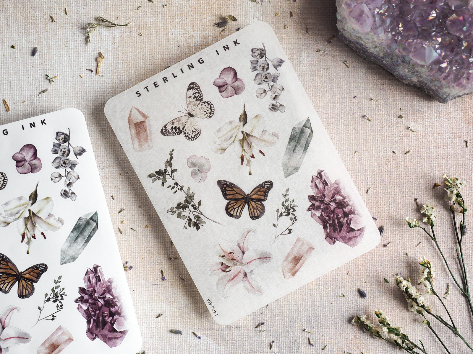 "Elements Stickers - April 2024" sticker sheet featuring delicate, muted watercolor illustrations of butterflies, floral bouquets, and raw crystal formations.