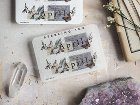 Decorative April month sticker featuring delicate butterflies amidst vintage botanical illustrations and subtle sketched blueprint elements.