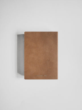 A slim, rectangular brown leather notebook or journal with a textured cover, standing upright against a light gray background.
#Color_Caramel