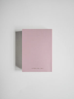 A minimalist pink notebook with a matte finish and a small black text logo at the bottom, displayed on a clean white background with a soft shadow.
#Color_Fairyfloss