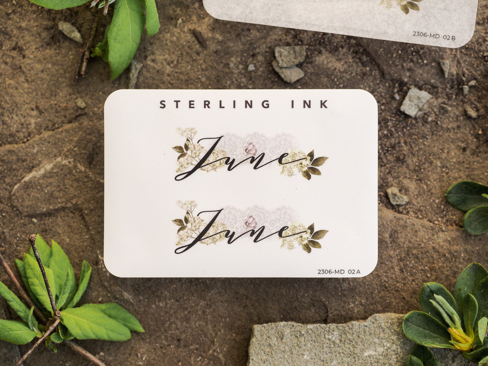 Elegant white planner sticker featuring the scripted word "June" surrounded by delicate watercolor green leaves and light floral accents for journaling and scrapbooking.