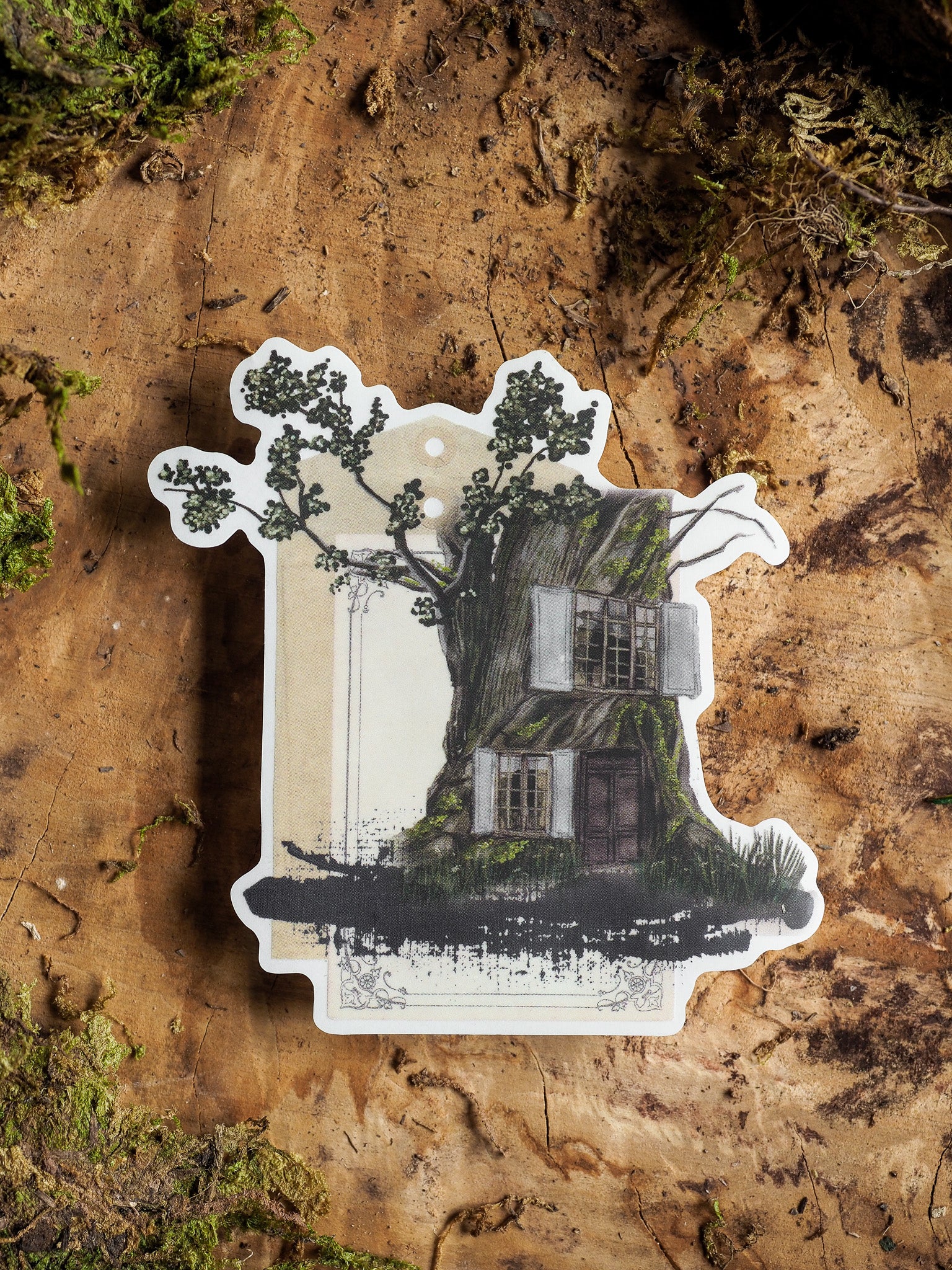Vintage illustration die-cut sticker depicting a charming, rustic cottage nestled among lush, stylized green trees and dense foliage.