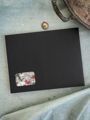 Minimalist black board displaying a delicate watercolor floral sticker with a vibrant botanical pattern in pink, red, and green tones.