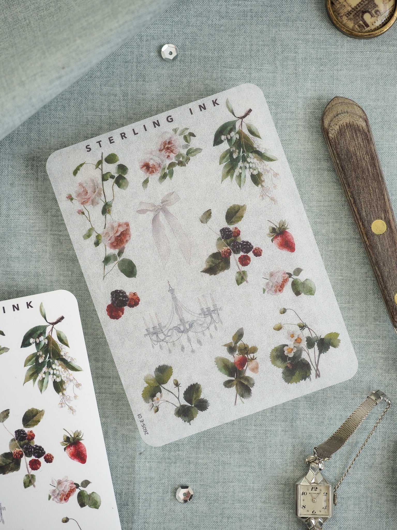 Watercolor botanical sticker sheet featuring an array of lush berries, green foliage, and delicate pink florals surrounding a detailed antique chandelier illustration.