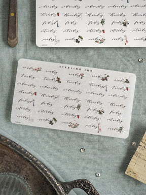 Decorative "Sterling Ink" label featuring repeating handwritten words and delicate red and green floral motifs, suitable for scrapbooking, journaling, or stationery decor.