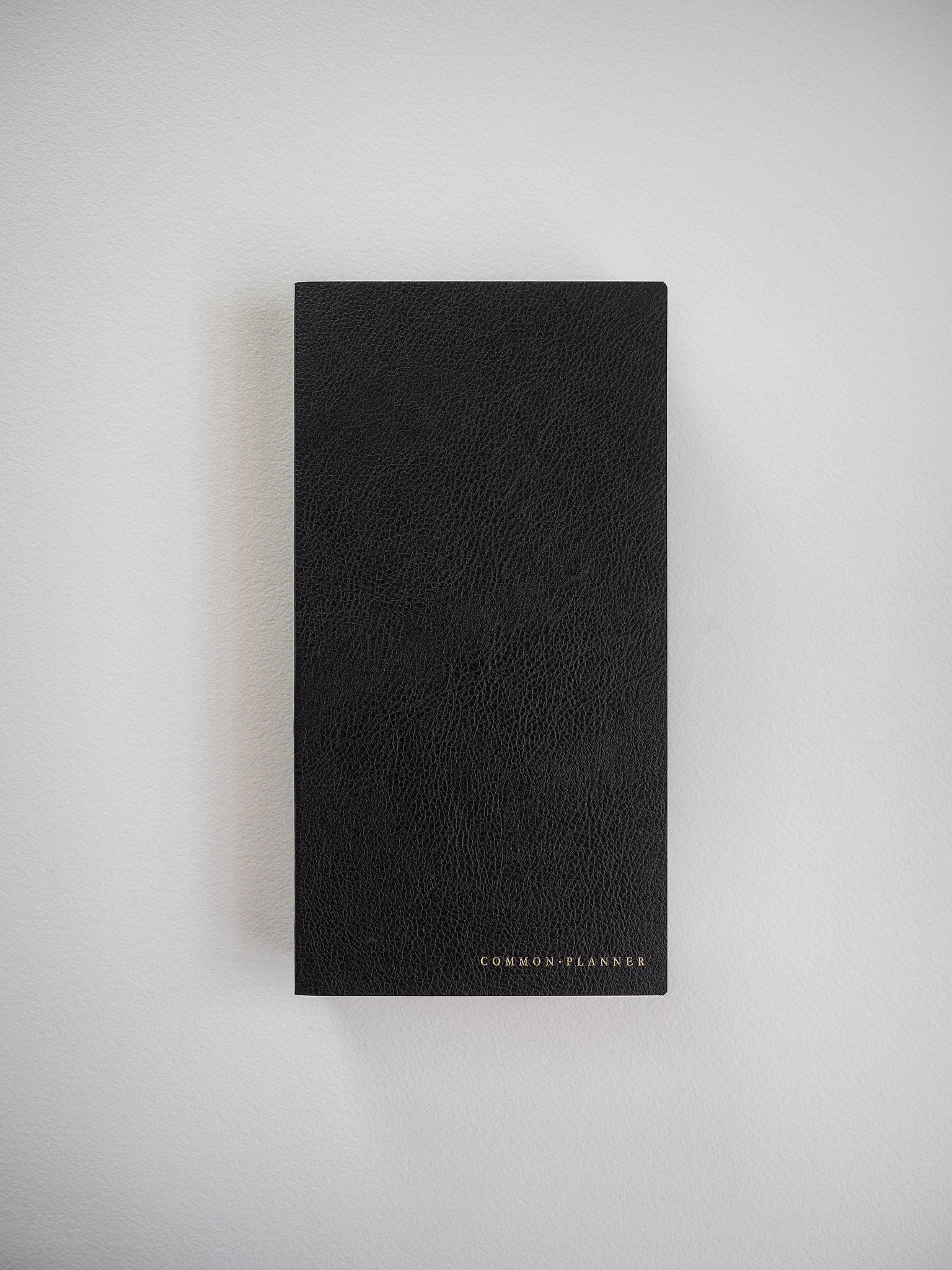 A compact, matte black planner featuring a textured, faux leather cover and minimalist "COMMON PLANNER" branding across the bottom.
