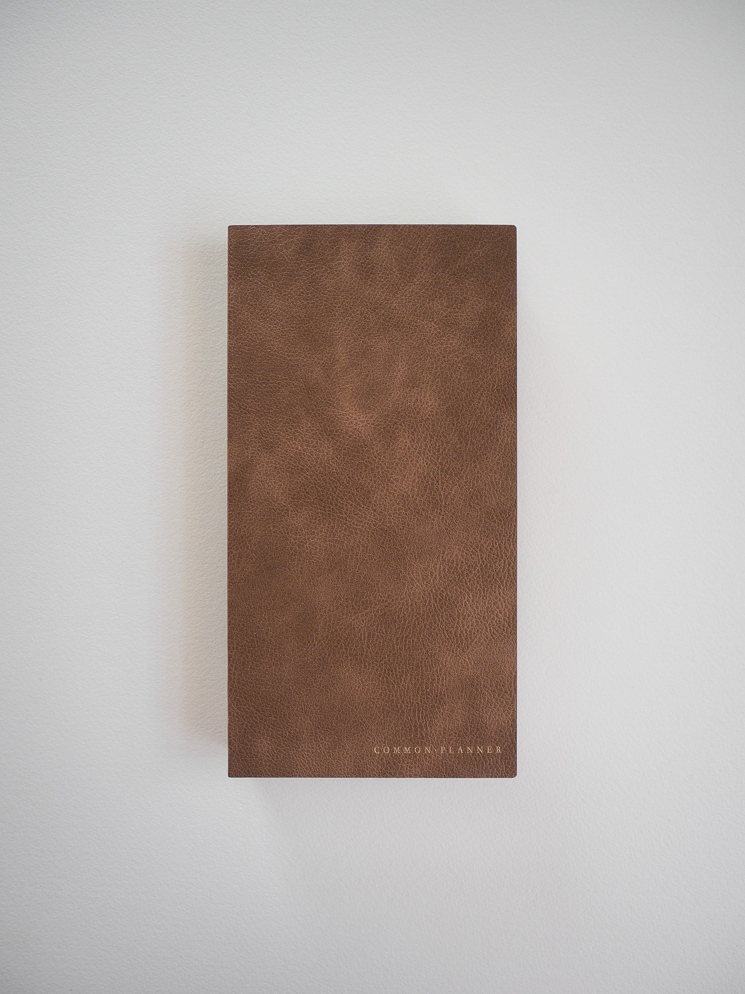 Rich brown, textured faux leather planner cover featuring the brand name "COMMON PLANNER" embossed near the bottom.