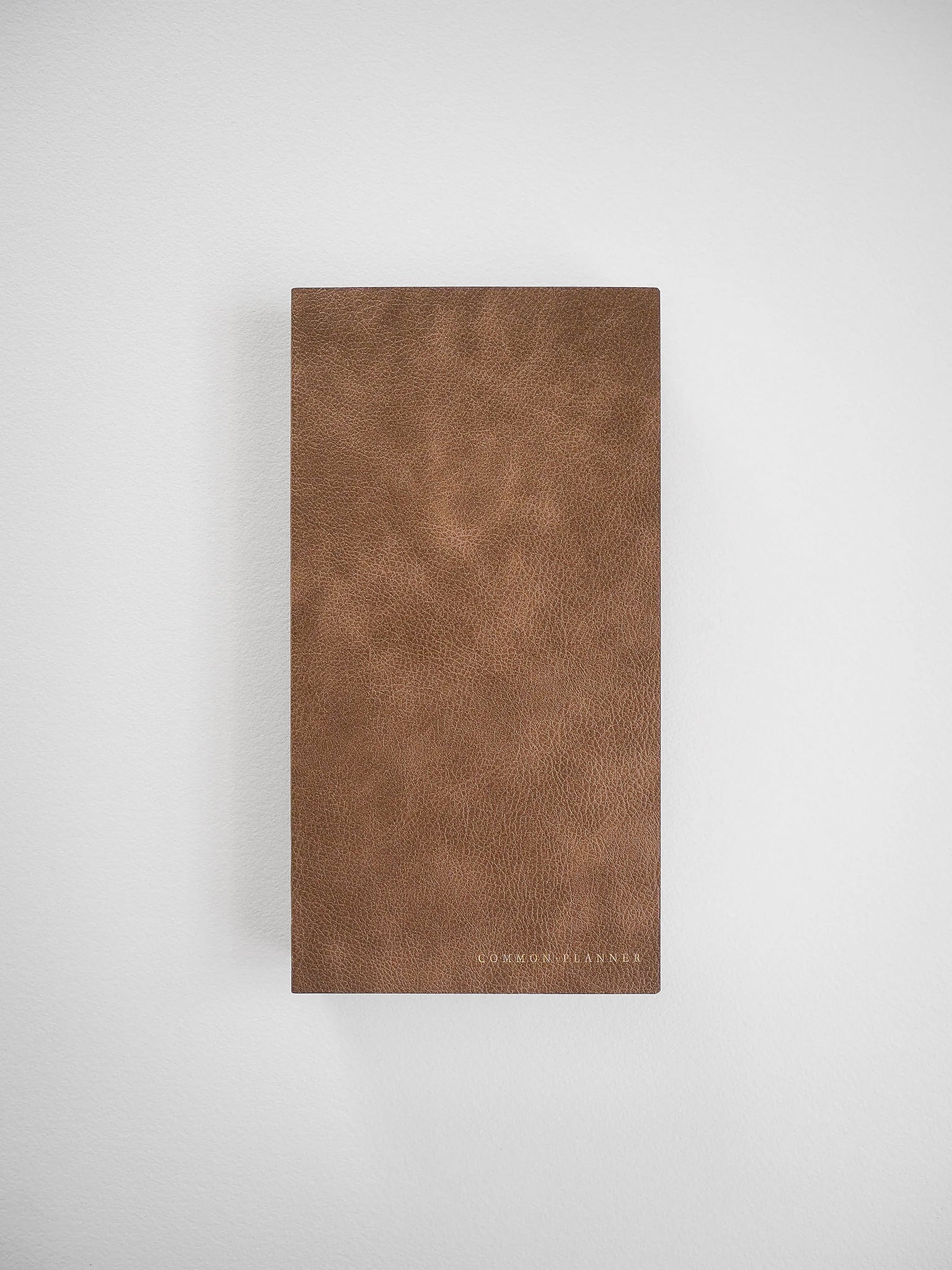 Deep tan, pebbled faux leather planner cover featuring a subtle grain texture and the "COMMON PLANNER" branding at the bottom.