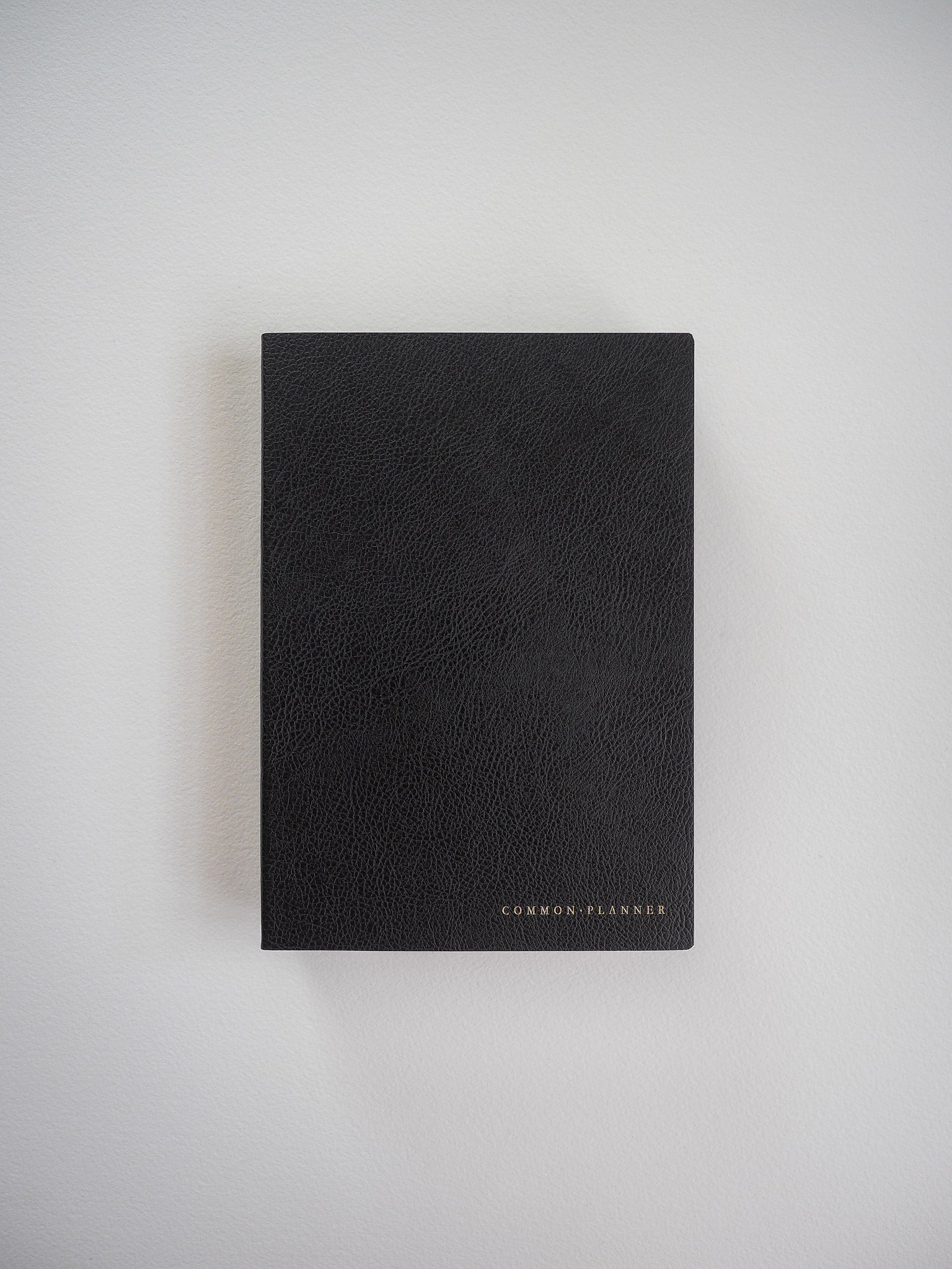 Compact, vertical black planner featuring a textured, faux-leather cover and subtly debossed "COMMON PLANNER" branding.