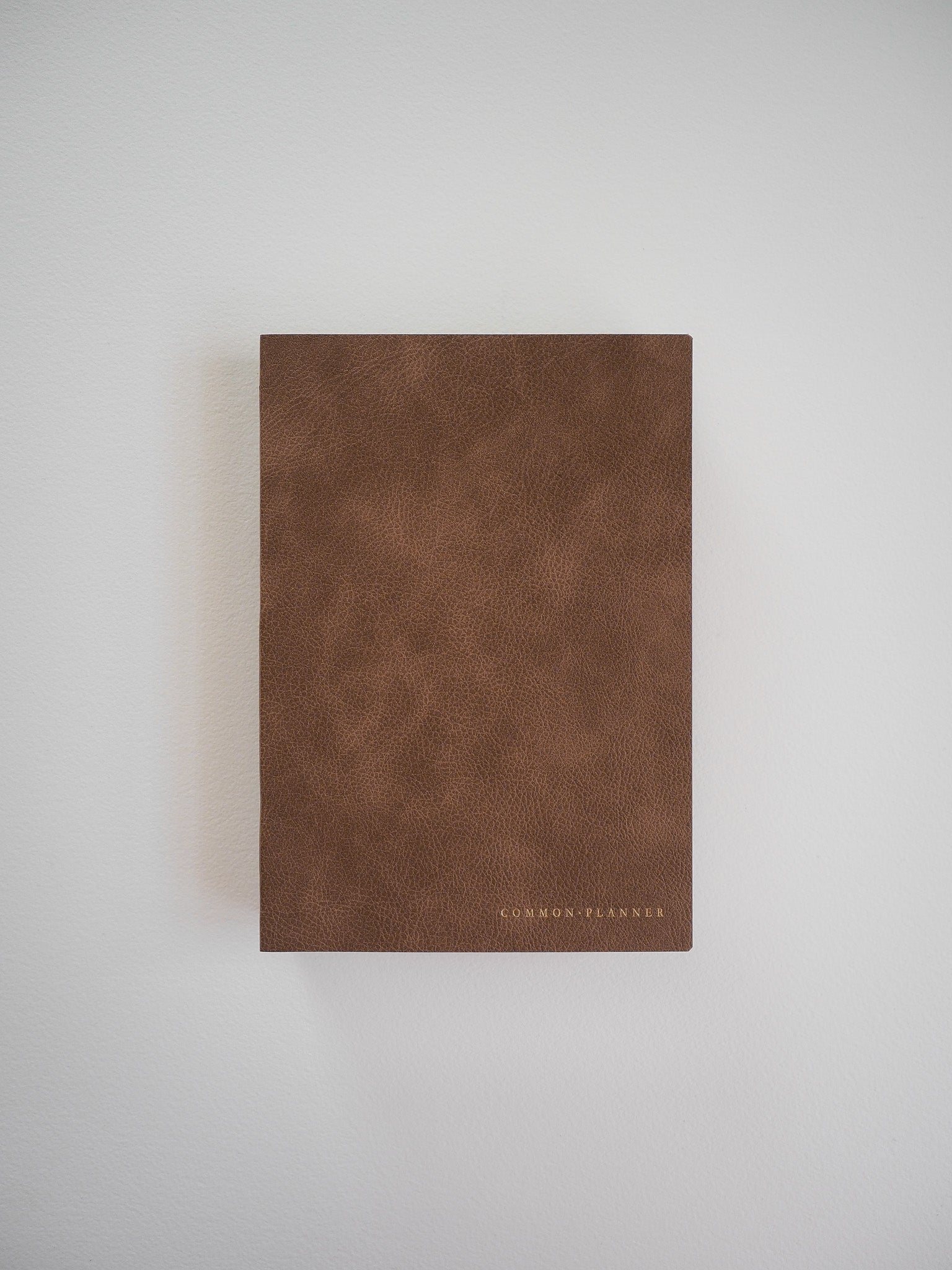 A minimalist, full-year undated planner with a rich, textured saddle brown cover and "COMMON PLANNER" subtly debossed near the bottom edge.
