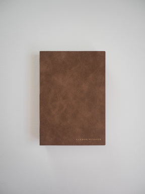 A minimalist, full-year undated planner with a rich, textured saddle brown cover and "COMMON PLANNER" subtly debossed near the bottom edge.