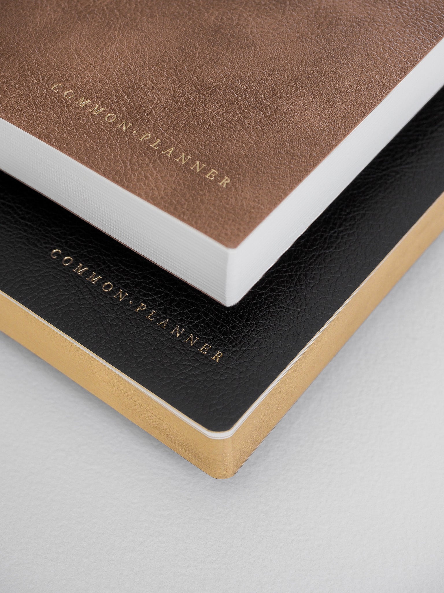 A stack of three A5 planners in coordinating tan, crisp white, and classic black covers, each featuring the embossed 'COMMON PLANNER' title.