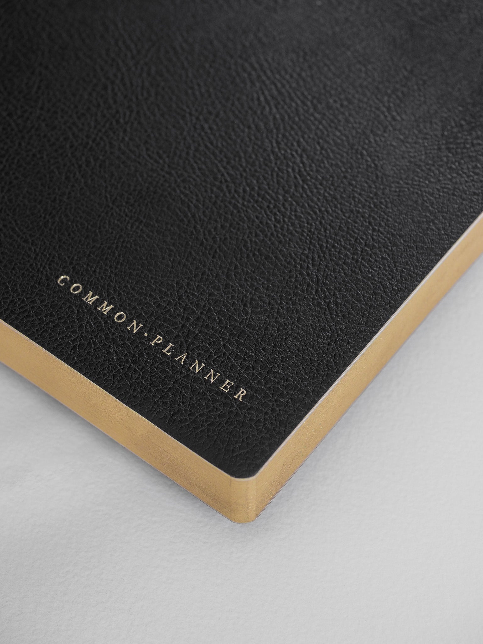 Sleek black planner cover featuring elegant metallic gold lettering that spells out 'Common • Planner' near the bottom edge.