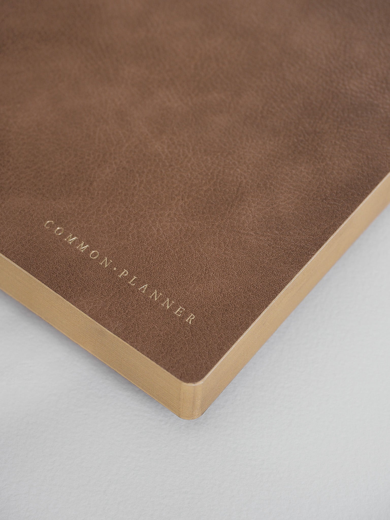Deep cocoa brown A5 planner cover with minimalist gold foil stamping displaying the brand name "COMMON • PLANNER."