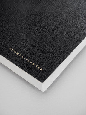 Dark black, textured faux-leather A5 planner featuring debossed branding that reads "COMMON PLANNER," perfect for year-long planning.