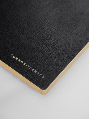 Minimalist dark gray planner cover featuring "COMMON PLANNER" in delicate gold foil lettering and accented with contrasting tan edges.