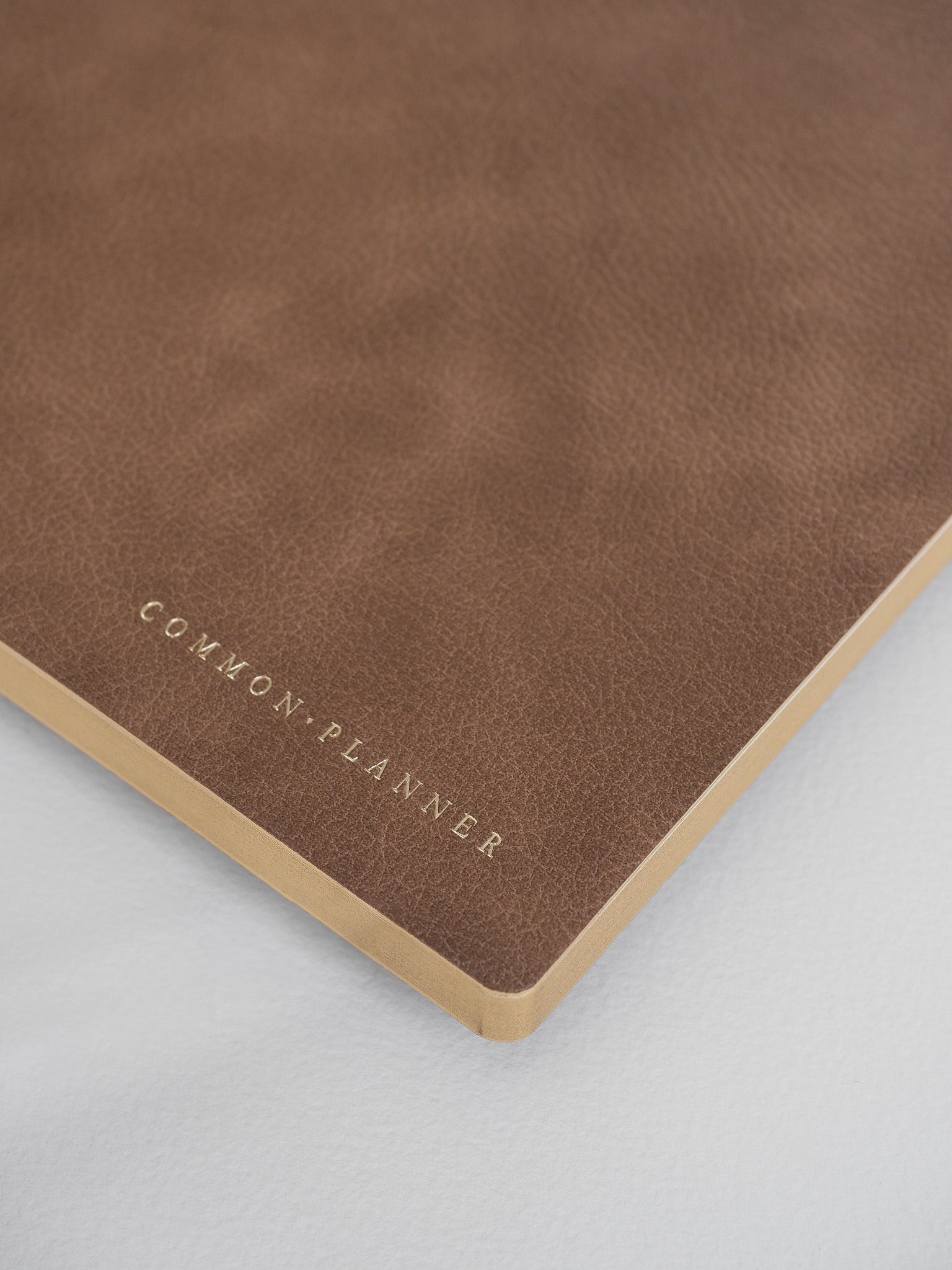 Minimalist taupe A5 planner featuring subtle metallic gold lettering that reads "COMMON PLANNER," perfect for an undated journal.