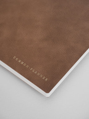 Matte, earthy brown common planner with debossed lettering that reads "COMMON PLANNER," offering a sophisticated and minimal look.