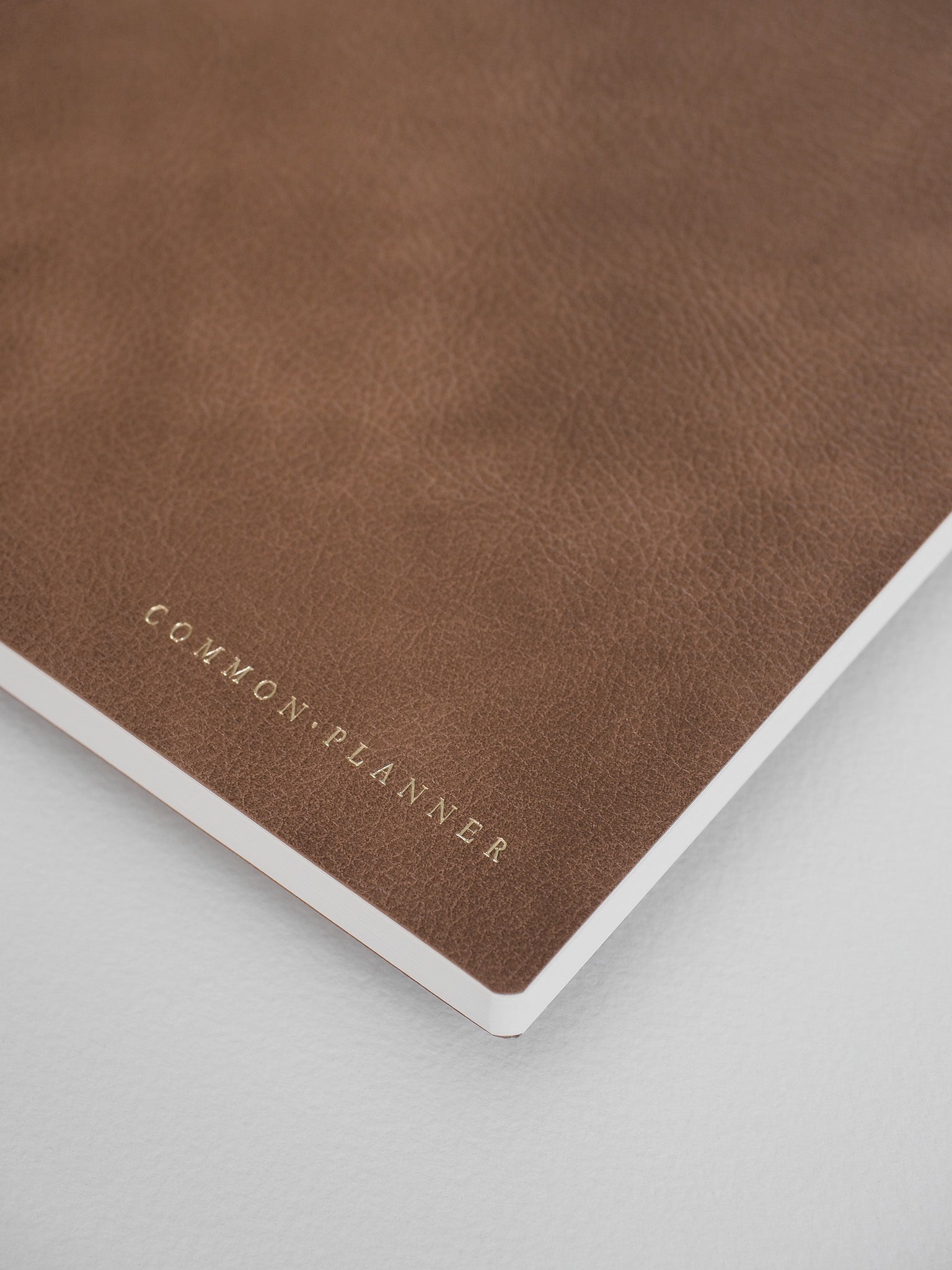 Deep brown, matte faux leather planner cover featuring the "COMMON PLANNER" brand name stamped in elegant metallic foil.