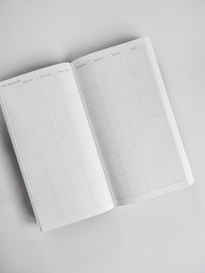 Open undated planner pages featuring a clean, structured grid layout with distinct sections for daily, weekly, monthly, and quarterly goal planning.