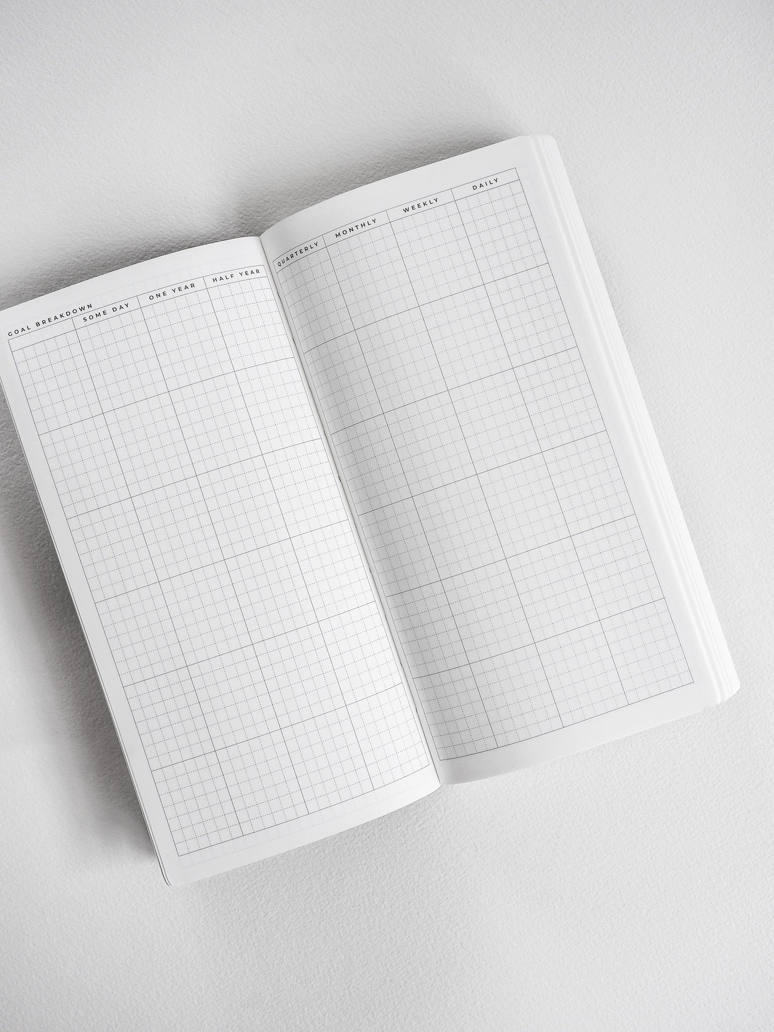 Open, neutral-toned undated planner showcasing a meticulously gridded layout with structured headers for goal breakdown, weekly, and monthly scheduling planning.