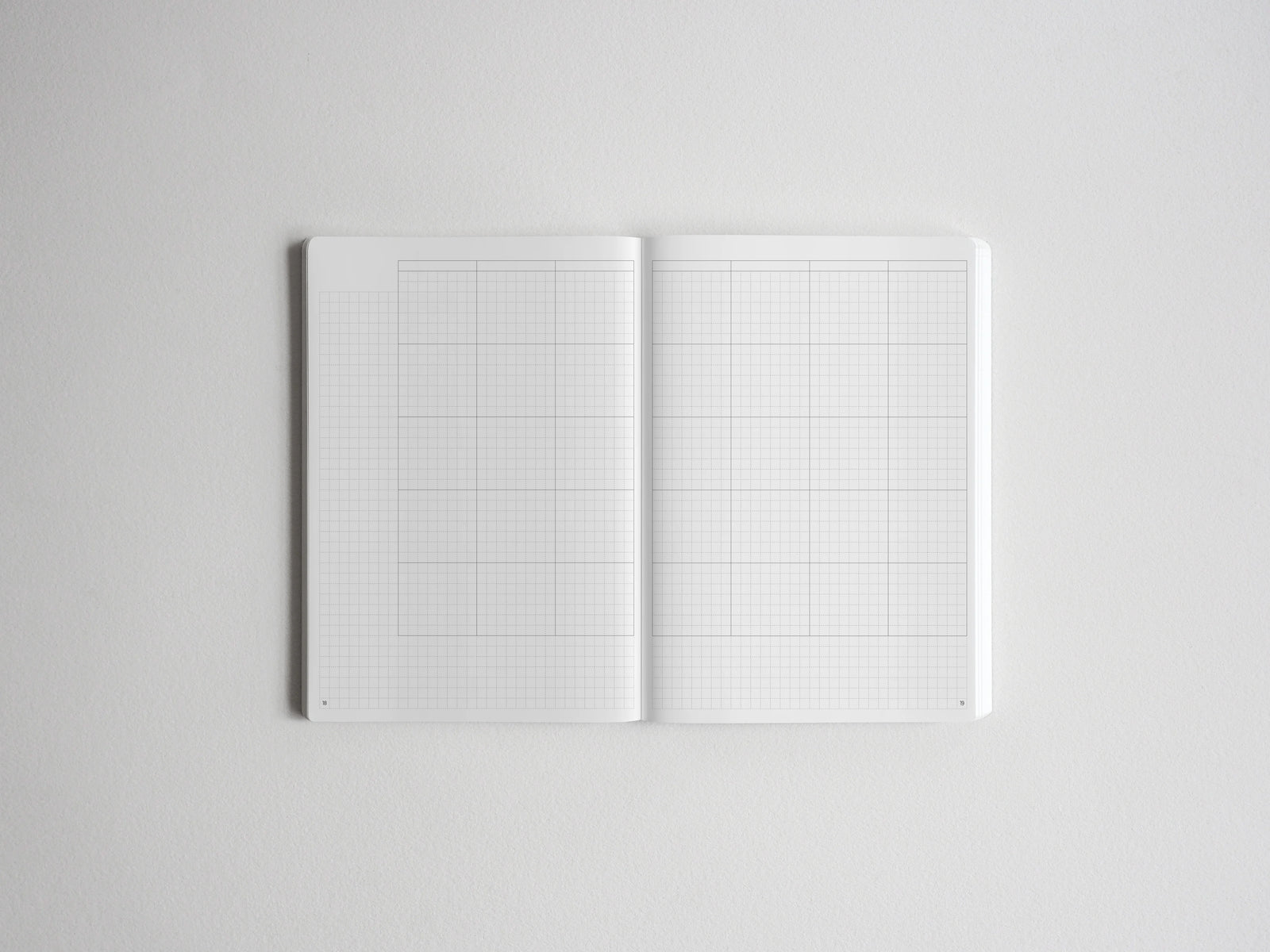 Open notebook spread showing two pristine white pages printed with fine graph paper grids, perfect for sketching, planning, or journaling.