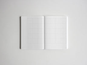 Open notebook spread showing two pristine white pages printed with fine graph paper grids, perfect for sketching, planning, or journaling.