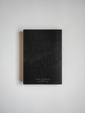 Sophisticated black B6 notebook featuring a subtle textured grain cover and minimalist white branding indicating its lined pages.