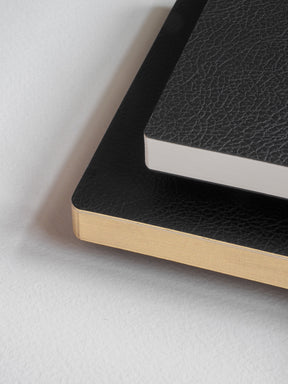 Deep black, textured pocket notebook featuring contrasting light gold edges and lined pages for writing notes.