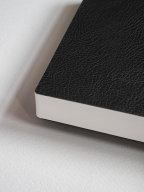 Black lined notebook featuring a smooth, pebble-textured cover and visible white edges, ideal for writing and journaling.