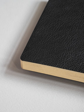Structured A5 notebook bound in light tan, featuring a sophisticated black cover with a refined, textured finish perfect for writing and journaling.