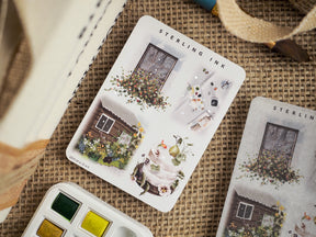 Detailed sticker sheets featuring whimsical illustrations of rustic cottages, overflowing floral arrangements, and vintage objects perfect for crafting.